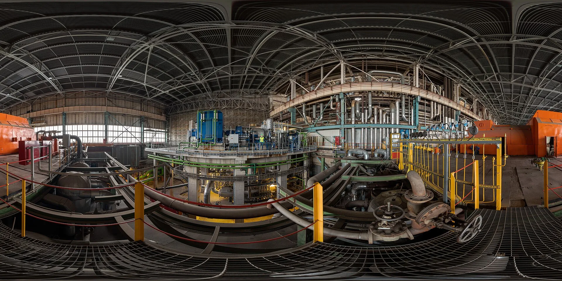 Una gran sala industrial con tuberías, pasarelas metálicas y cubierta de acero, en blanco y negro con un tono verde.